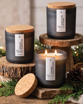 Aspen & Oak beeswax candles in frosted glass jars with cork lids, including a lit Pumpkin Spice Bourbon, styled with evergreen, pinecones and dried orange slices for the holidays